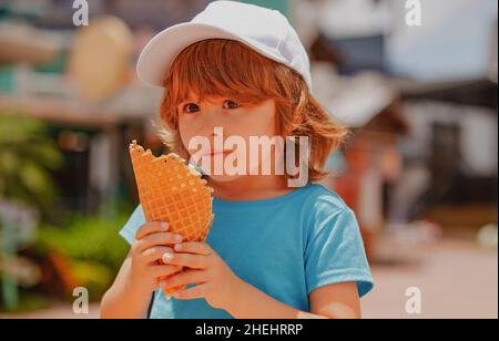 Enfant mangeant de la glace. Un petit garçon heureux qui mange de la glace à l'arrière-plan de la ville. Banque D'Images