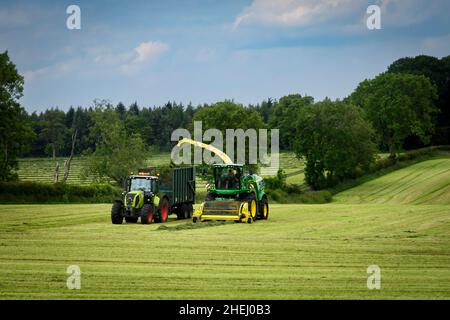 1 production de foin de tracteur Claas, travail dans les champs agricoles, conduite avec une remorque de remplissage d'ensileuse John Deere (ensilage d'herbe coupée) - Yorkshire, Angleterre, Royaume-Uni. Banque D'Images