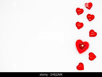 Une bougie rouge en forme de coeur et quelques coeurs en verre sont couchés sur une rangée à gauche.Concept d'amour, Saint-Valentin, passion.Copier la flèche Banque D'Images