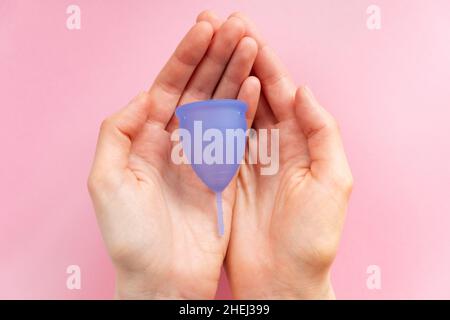 Les mains des jeunes femmes tiennent la coupe menstruelle en silicone violet contemporain sur fond rose clair très proche vue d'en haut Banque D'Images