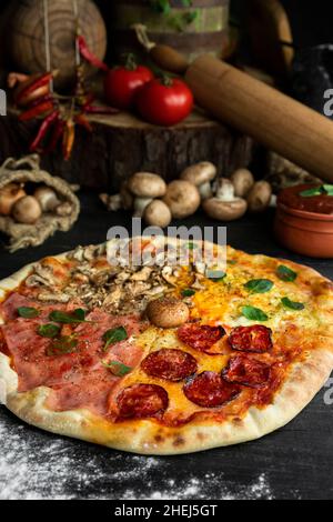 Pizza italienne four Seasons (Pizza Quattro Stagioni) avec différents ingrédients sur la table en bois dans la cuisine.Recettes italiennes faites maison Banque D'Images