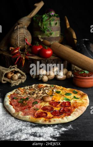 Pizza italienne four Seasons (Pizza Quattro Stagioni) avec différents ingrédients sur la table en bois dans la cuisine.Recettes italiennes faites maison Banque D'Images