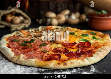 Pizza italienne four Seasons (Pizza Quattro Stagioni) avec différents ingrédients sur la table en bois dans la cuisine.Recettes italiennes faites maison Banque D'Images