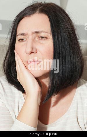 Femme d'âge moyen mature touchant la bouche avec la main souffrant de maux de dents à la maison.Concept de santé dentaire.Carie dentaire, inflammation ou dents sensibles Banque D'Images