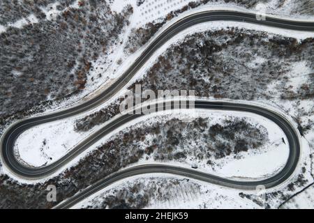 Image de drone de vue aérienne à grand angle sur la spirale incurvée route à travers les arbres et la forêt dans la chaîne de montagne avec Neige blanche en hiver près de Knja Banque D'Images