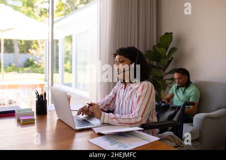 Femme afro-américaine handicapée en fauteuil roulant utilisant un ordinateur portable tout en travaillant de la maison Banque D'Images