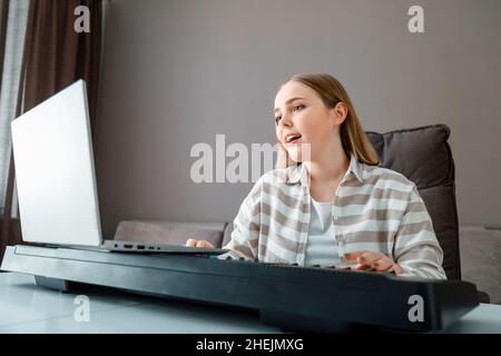 Femme apprend de la musique chantant des voix jouant du piano en ligne à l'aide d'un ordinateur portable à l'intérieur de la maison.Adolescente chante la chanson et joue le piano synthétiseur pendant Banque D'Images