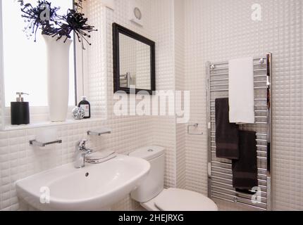 Lavabo, toilettes et porte-serviettes avec de petits murs carrelés blancs dans une nouvelle maison moderne. Banque D'Images