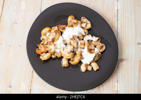 Champignons de Paris frits à la crème sure et à l'ail, sur une assiette noire irrégulière, vue du dessus Banque D'Images