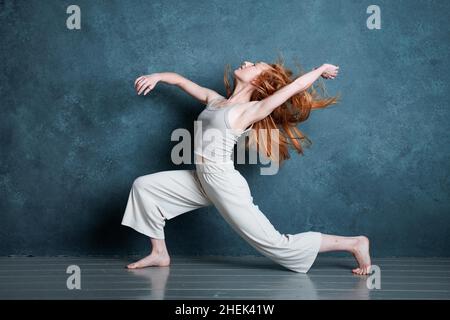 Danseuse Petitie avec des cheveux auburn rouges dansant sur fond gris Banque D'Images