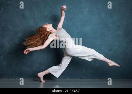 Danseuse Petitie avec des cheveux auburn rouges dansant sur fond gris Banque D'Images