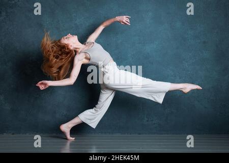 Danseuse Petitie avec des cheveux auburn rouges dansant sur fond gris Banque D'Images