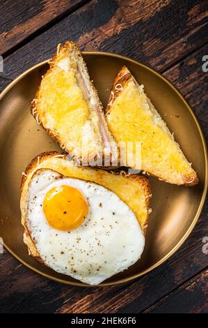 Toasts français croque monsieur et croque madame, sandwichs grillés sur pain de brioches avec tranches de jambon, fromage emmental fondu et œuf.Arrière-plan en bois Banque D'Images