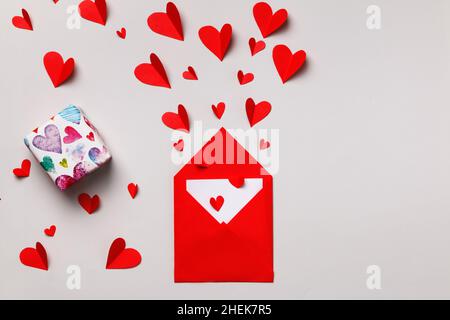 Lettre d'amour pour la Saint-Valentin.Enveloppe en papier rouge avec une note à l'intérieur, boîte avec un cadeau et des coeurs sur fond gris pastel. Banque D'Images