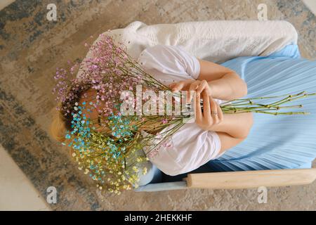 Vue d'en haut sur une femme assise dans un fauteuil avec fleurs de printemps à la main Banque D'Images