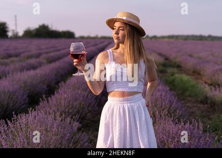 Belle fille avec un verre de vin rouge dans un champ de lavande en Provence d'été.Alcool dans la nature et aromathérapie.Repos et détente à l'extérieur. Banque D'Images