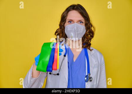 Femme médecin tient des bandes élastiques de forme physique sur un fond jaune, gros plan. Banque D'Images