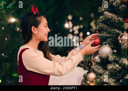 Joyeuse femme asiatique portant un bandeau de bois décorant boule d'ornement sur arbre de noël la nuit Banque D'Images