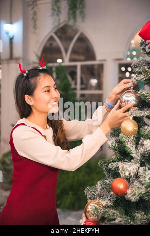 Joyeuse femme asiatique portant un bandeau de bois décorant boule d'ornement sur arbre de noël la nuit Banque D'Images