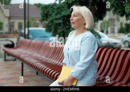 Adulte 50 ans enseignante femme sur un banc en bois dans un parc tenant des livres Banque D'Images