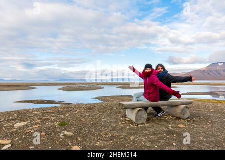 Vue arrière portrait d'un jeune couple assis sur un banc, jeune couple en vacances - svalbard, paysage arctique Banque D'Images