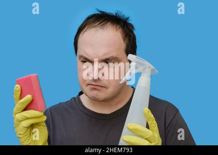 Doutant homme nettoyant en gants jaunes , portrait sur fond bleu studio Banque D'Images