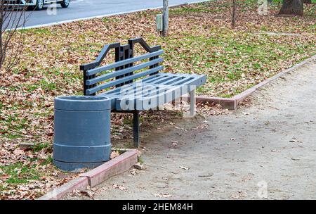 Un banc en bois peint en gris et une poubelle dans un parc d'automne près du sentier. Banque D'Images