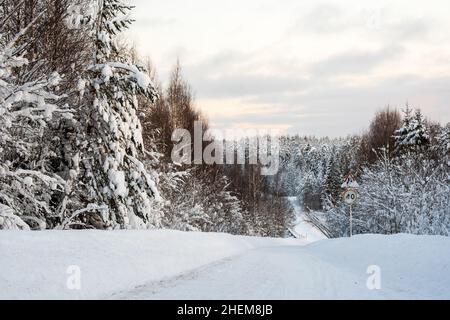 Route de campagne dégagée de neige avec une descente abrupte vers un pont avec un lac gelé, au milieu d'une forêt enneigée. Banque D'Images