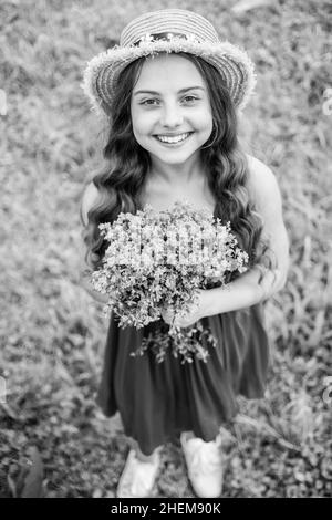 Joyeux bébé fille porter un chapeau de soleil sur les cheveux à long chemin et la mode robe d'été tenant des fleurs paysage naturel, boutique florale Banque D'Images