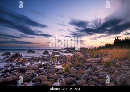 Longue exposition de magnifique coucher de soleil doux et coloré par la pierre du bord de mer. Magnifique mouvement de nuages avec pierres de mer. Banque D'Images