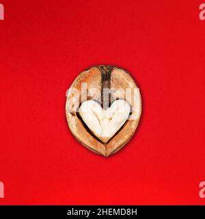 Drôle minimaliste Saint Valentin concept, ouvert moitié de noyer avec noyau qui ressemble à coeur ou hibou visage sur rouge Banque D'Images