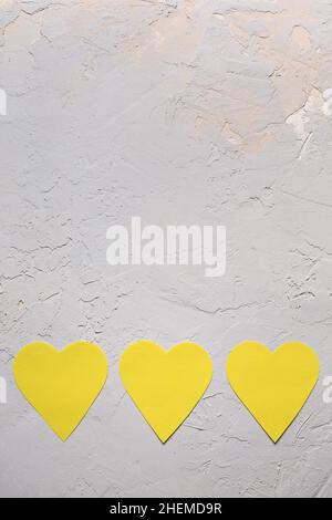 Carte de vœux minimaliste pour la Saint-Valentin en gris ultime et couleurs jaune illuminées de l'année 2021, trois coeurs en papier sur fond texturé Banque D'Images