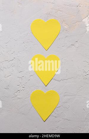 Carte de vœux minimaliste pour la Saint-Valentin en gris ultime et couleurs jaune illuminées de l'année 2021, trois coeurs en papier sur fond texturé Banque D'Images