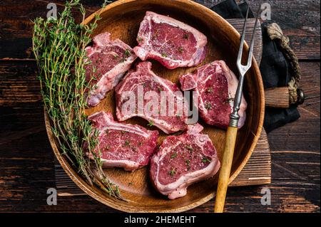 Côtelettes de longe d'agneau crues steaks dans un plat en bois aux herbes.Arrière-plan en bois.Vue de dessus Banque D'Images