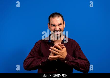 Homme caucasien en chemise violette isolé sur fond bleu avec les doigts couverts et semble mystérieux au côté a un grand plan de mal à l'esprit Banque D'Images