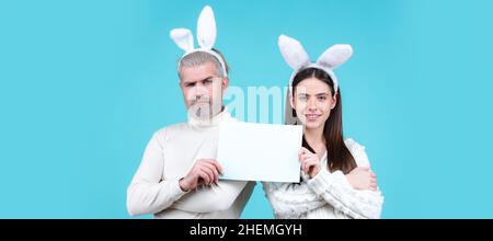 Le couple de Pâques tient un tableau blanc vierge pour votre texte.Bannière avec un couple de lapins drôle, espace de copie. Banque D'Images