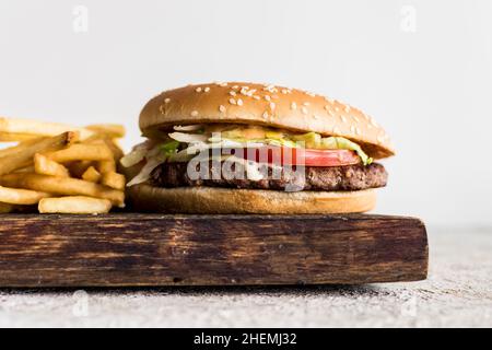 Gros plan de gros hamburger maison savoureux avec du bœuf, du fromage, des tomates, de la laitue et des frites sur une planche de bois sur un bakrok blanc.Hamburger savoureux contre hamburger laid. Banque D'Images