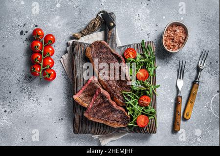 Steak de viande de bœuf rôti au chapeau ou au sirloin supérieur sur une planche de bois avec salade.Arrière-plan gris.Vue de dessus Banque D'Images