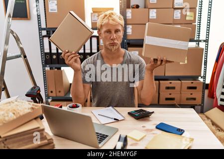 Jeune homme blond tenant des paquets travaillant à la boutique en ligne déprimé et s'inquiéter de la détresse, pleurant en colère et peur. Expression triste. Banque D'Images