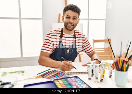 Jeune artiste arabe homme souriant dessin heureux au studio d'art. Banque D'Images