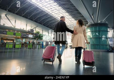 Pleine longueur de deux personnes, homme et femme, jeune couple avec des valises marchant le long du hall de départ de l'aéroport international sur le flou Banque D'Images