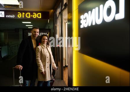 Partenaires d'affaires, couple multiracial d'une femme d'âge moyen et d'un homme avec des valises souriant regardant l'appareil photo à l'entrée de la zone hors taxes de Banque D'Images