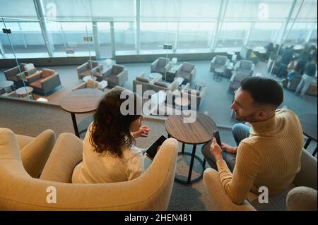 Vue aérienne d'un jeune couple multiracial contemporain amoureux, lors d'un voyage de lune de miel discutant du vol à venir en attendant le départ de l'avion Banque D'Images