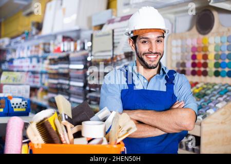 Workman debout bras pliés près du panier avec les outils ramassés dans le magasin de peinture Banque D'Images