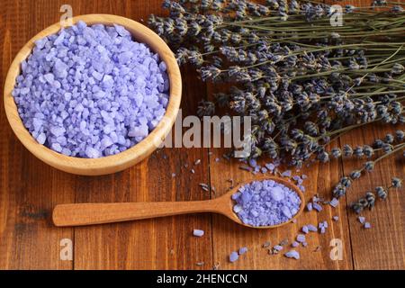 Le sel de mer à la lavande dans un bol en bambou et dans une cuillère en bois et les fleurs de lavande séchées sont situés sur une table en bois marron.Gros plan.Vue de dessus vers le bas. Banque D'Images