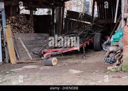 Un hangar dans le village avec une remorque en métal pour le bois et d'autres articles ruraux Banque D'Images