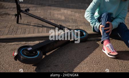 Une femme de race blanche est tombée d'un scooter électrique et a blessé sa jambe.Souffrant de douleur. Banque D'Images