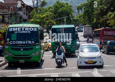 Medellin, Antioquia, Colombie - novembre 11 2021 : Latino-femme attend aux feux de signalisation sur une moto par deux bus verts Banque D'Images
