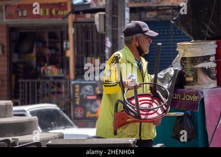 Medellin, Antioquia, Colombie - novembre 11 2021 : le vieil homme avec le chapeau, la veste jaune et le masque de visage déplace une chaise dans son stand Banque D'Images