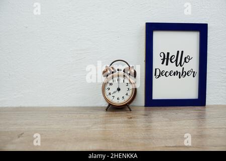 Texte typographique Hello December avec réveil sur table en bois et arrière-plan mural blanc Banque D'Images